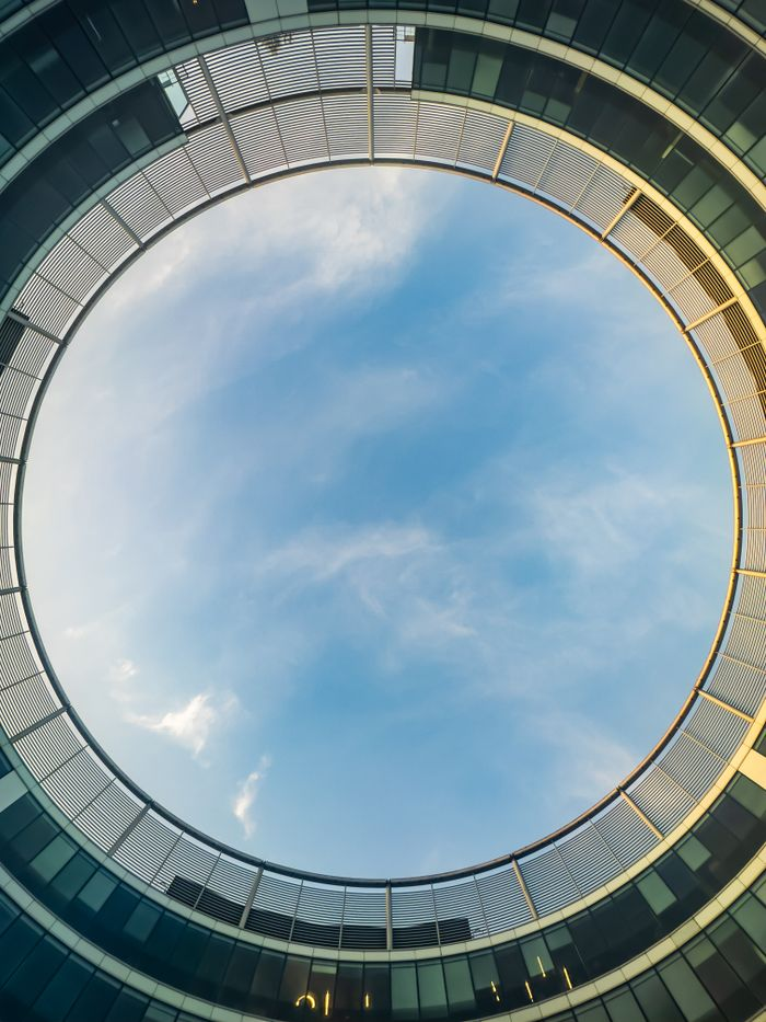 Circular view of the sky through a modern architectural structure with glass facade.
