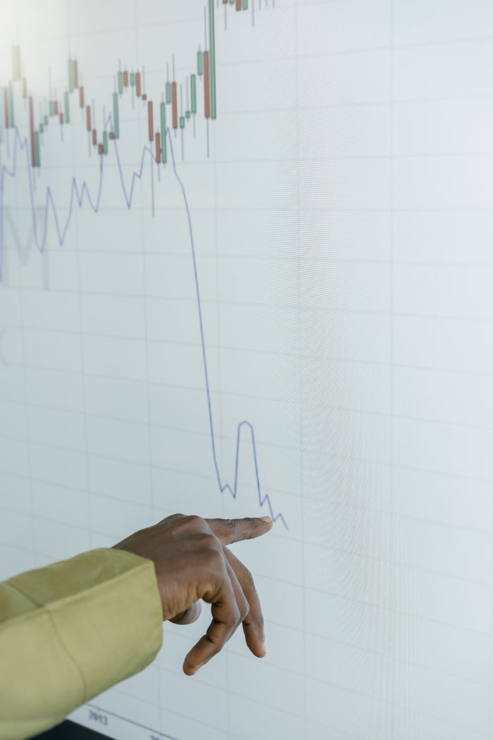 A person's hand accurately points to a significant drop on a financial stock graph displayed on a screen.